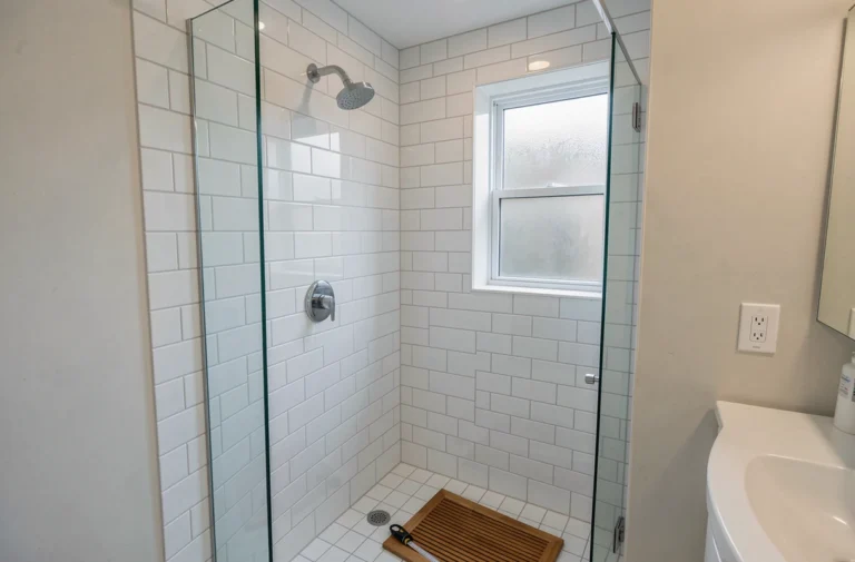 Douche à l'italienne avec carrelage blanc dans une salle de bain de location standard, vue grand angle